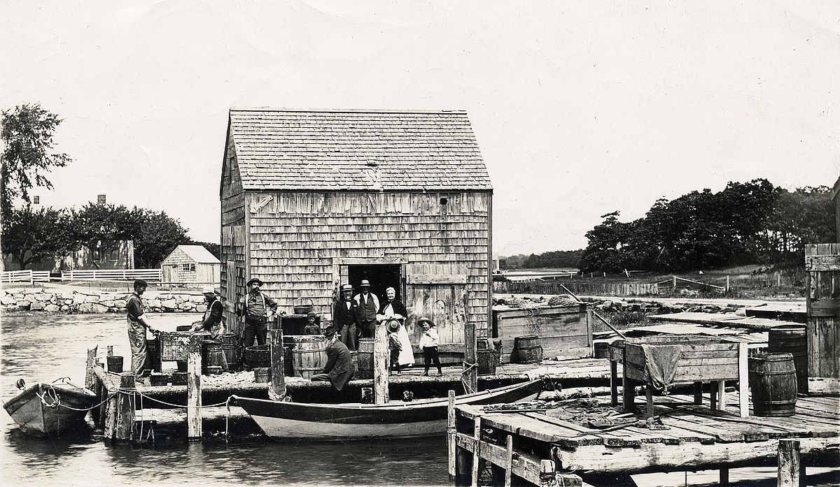Henry Hutchin’s fish house on the Pier Road, C. 1898. L to R: Merton Hutchins, Pharaoh Perry, Dana Cluff, child & two men unknown, Henry Hutchins (sitting—father of Merton Hutchins), Clara Pinkham Stone (Tom Bradbury’s great-grandmother) with twin sons Carl & Earl (Tom Bradbury’s grandfather) Stone